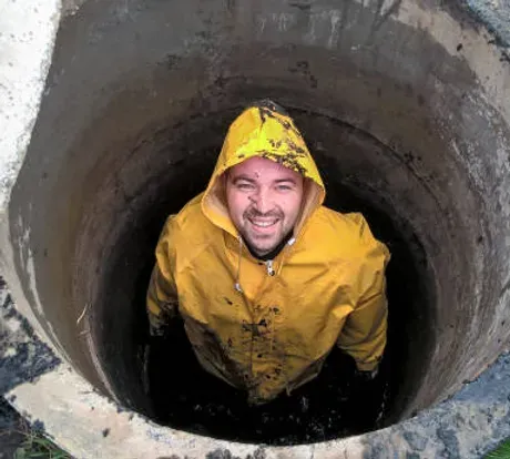 A man in a yellow raincoat is standing in a manhole.