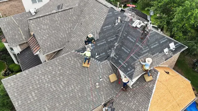 Roofers working on a house roof. They are wearing safety gear and installing new shingles.