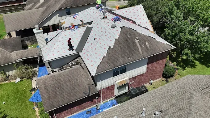 Roofers working on a house roof. Blue tarps cover portions of the house.