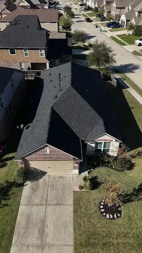 Overhead view of a suburban house with a dark roof and a driveway, surrounded by green lawns.