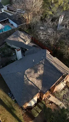 Overhead view of a house with a gray roof and a swimming pool in the background.