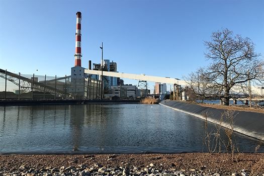 A large factory with a red and white chimney next to a body of water.