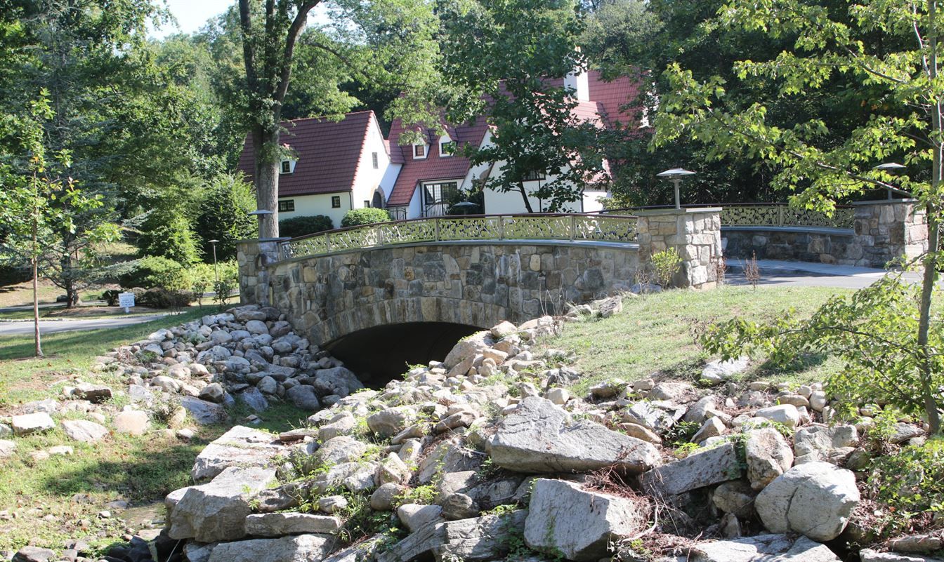 A stone bridge over a stream with a house in the background