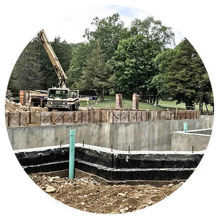 A concrete foundation is being built in a dirt field with trees in the background.