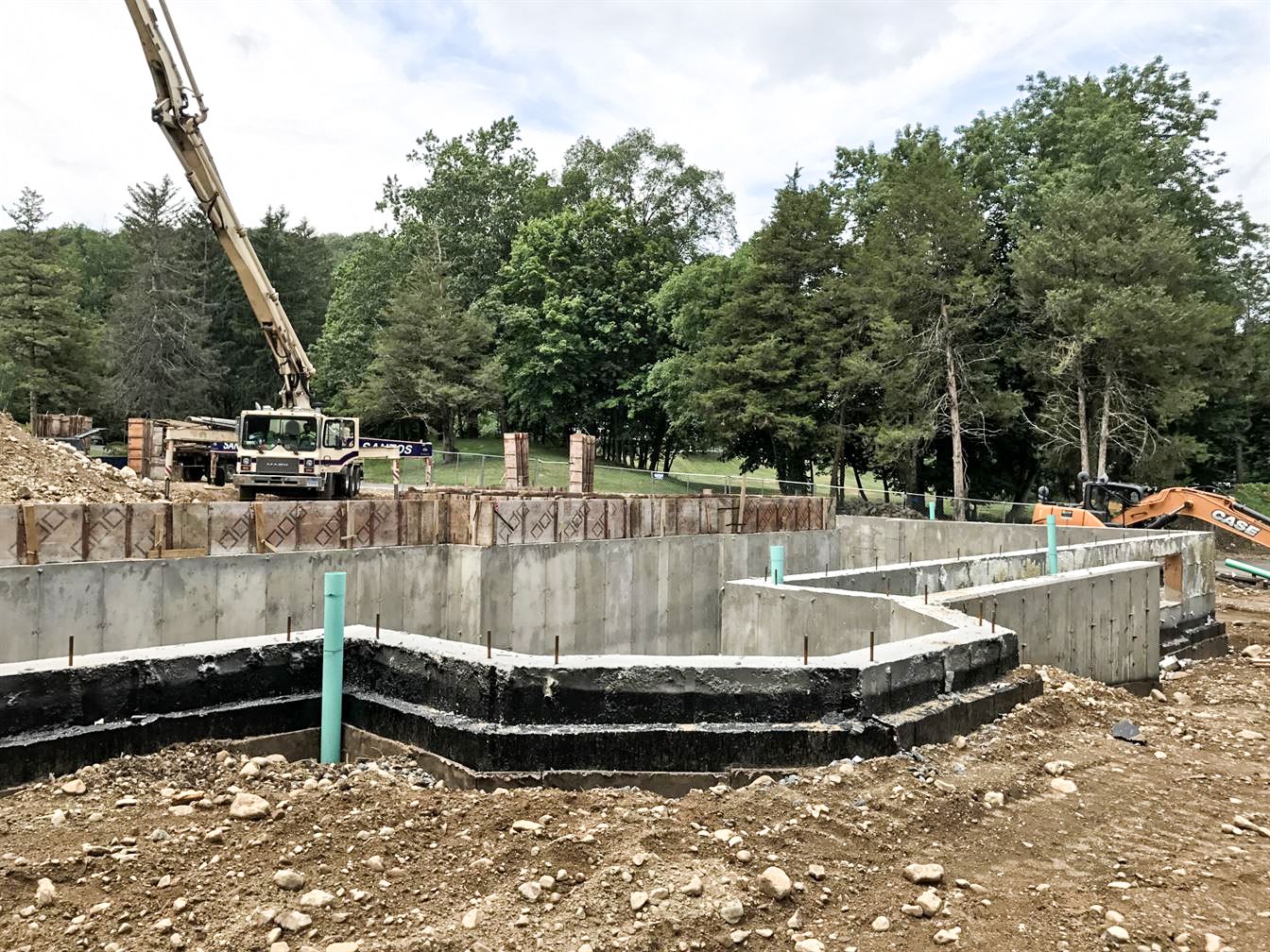 A concrete foundation is being built in a dirt field with trees in the background.