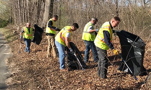 A group of men are picking up trash on the side of a road.