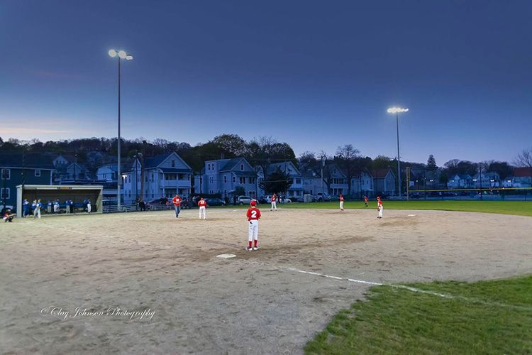 A young boy is standing on a baseball field at night.
