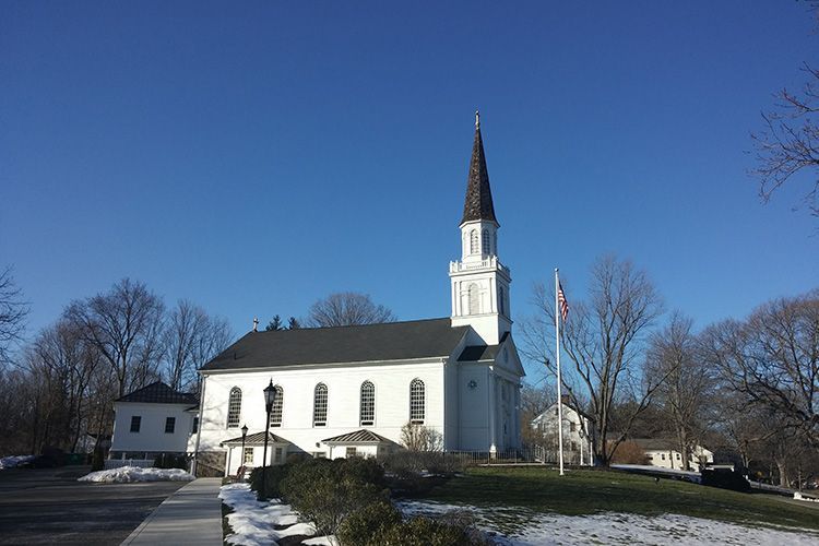 A white church with a steeple and a flag in front of it.