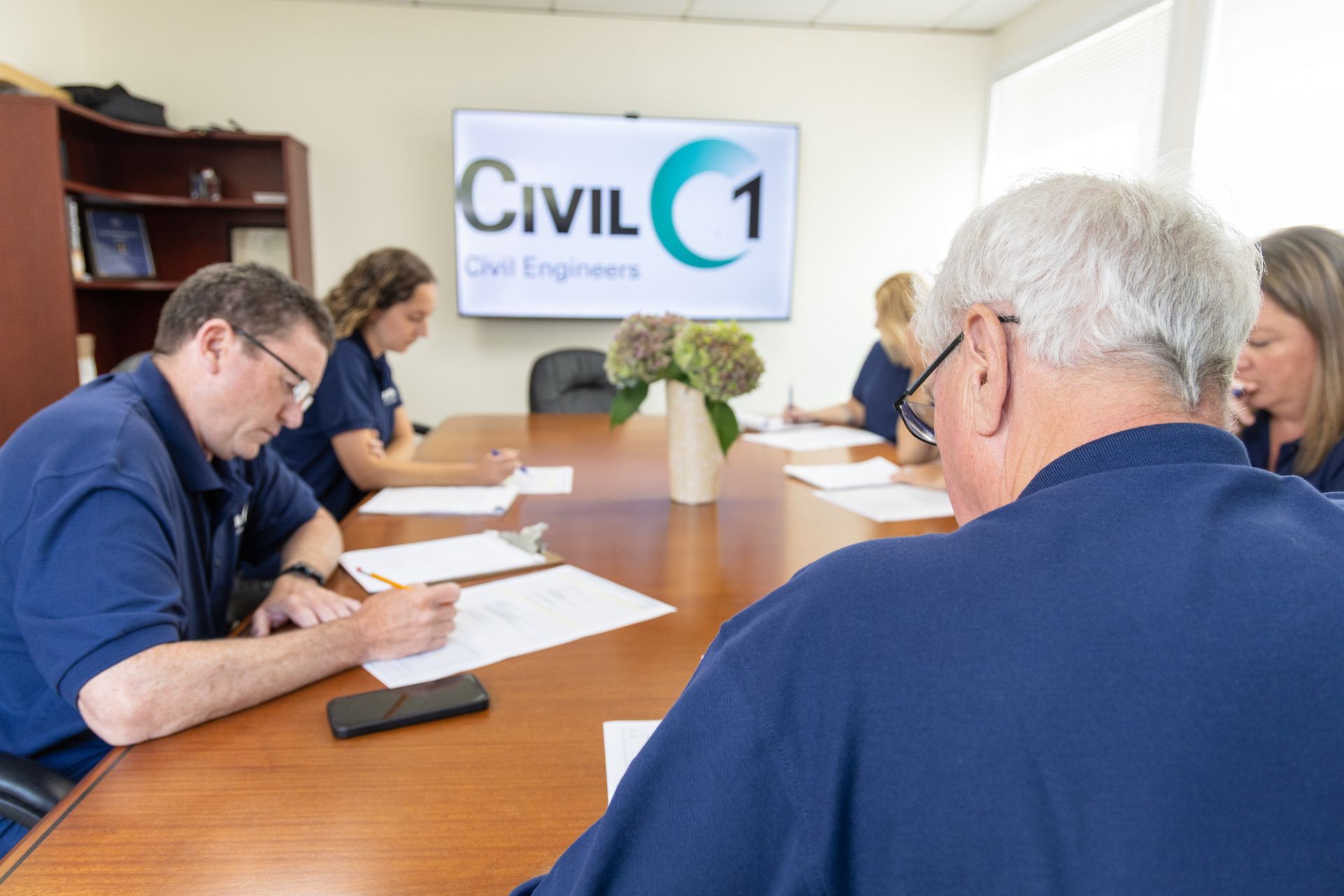 Small business meeting in a conference room with people reviewing papers and a “CIVIL 1” sign on the wall.
