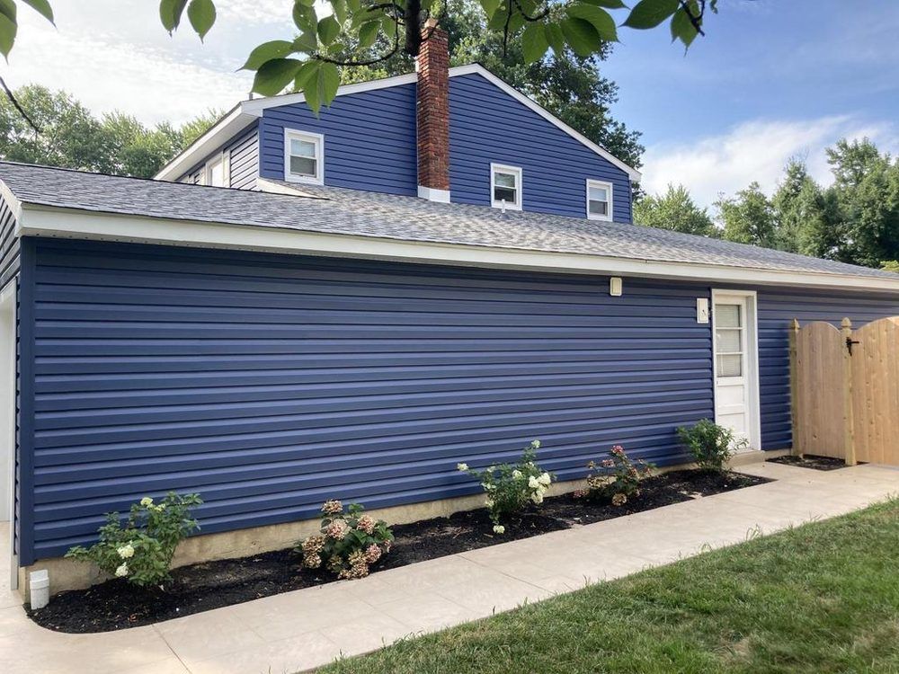Blue house exterior with white trim, landscaped flower bed, and wooden fence along a concrete walkway