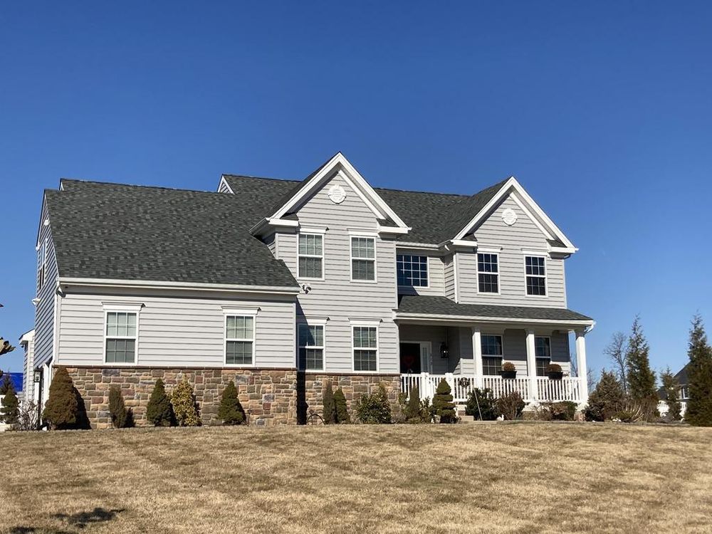Large gray suburban house with a dark roof on a grassy hill under a clear blue sky