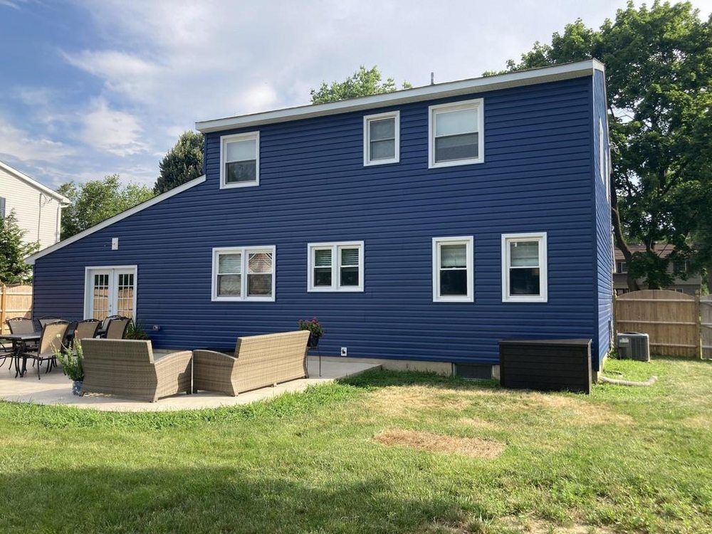 Blue two-story house with white trim and a backyard patio set on a grassy lawn