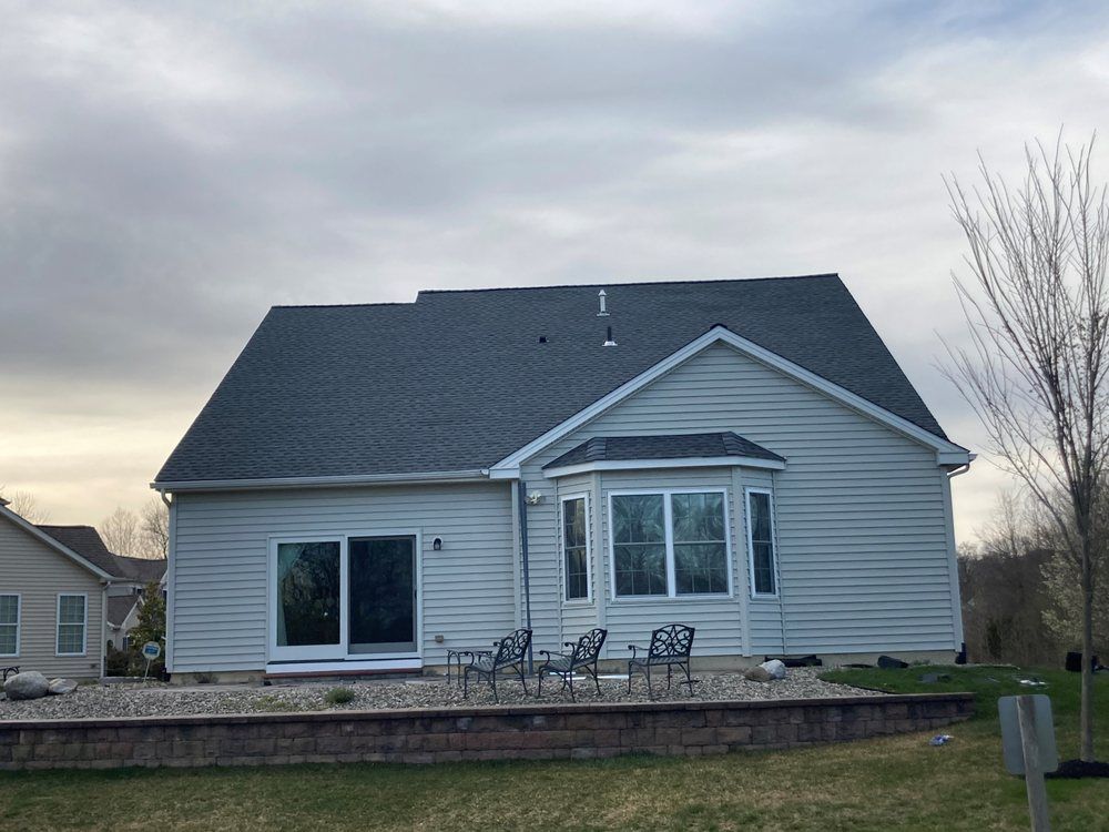 Gray house with white trim and stone patio at dusk, with outdoor chairs in front yard.
