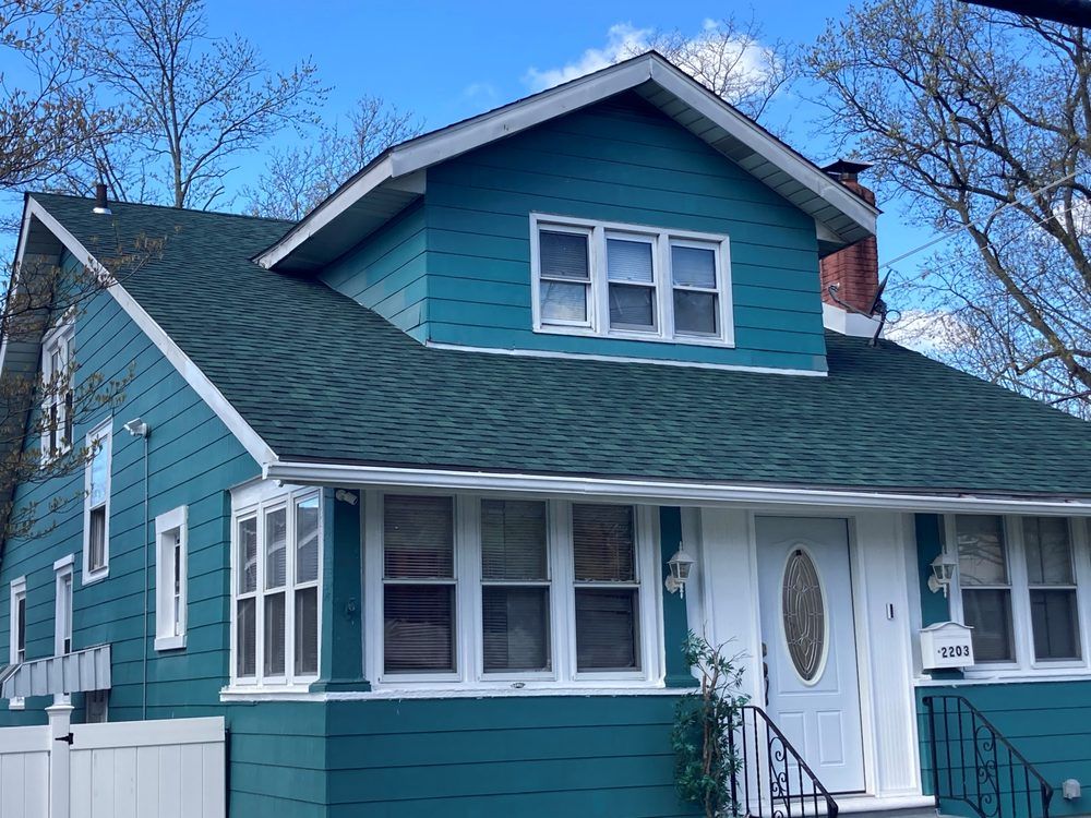Blue two-story house with white trim, front porch, and a steep green roof under a clear sky