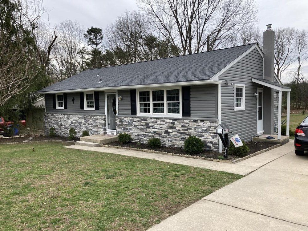 Single-story gray stone house with dark roof, front lawn, and concrete driveway.