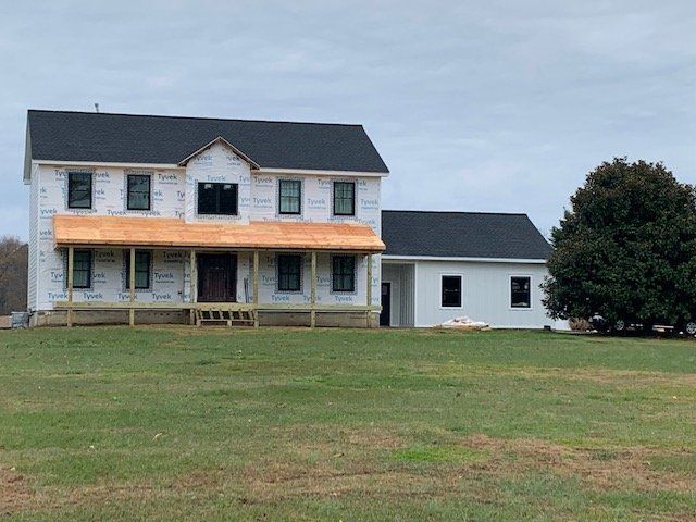 White two-story farmhouse with dark roof and orange porch awning on a grassy lawn