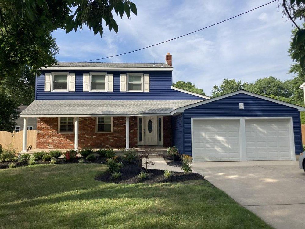Two-story blue house with white trim and detached two-car garage, front lawn and porch