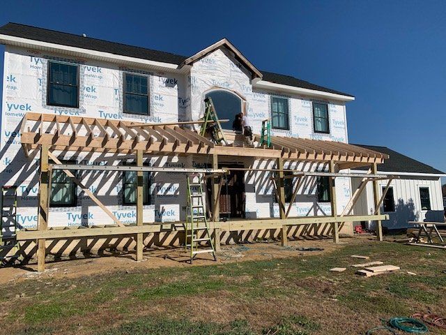 Two-story house under construction with white siding, a wooden deck frame, and blue sky.