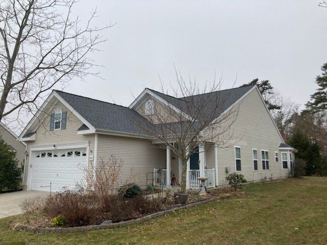 Suburban beige house with attached garage, gray roof, and leafless trees in front yard