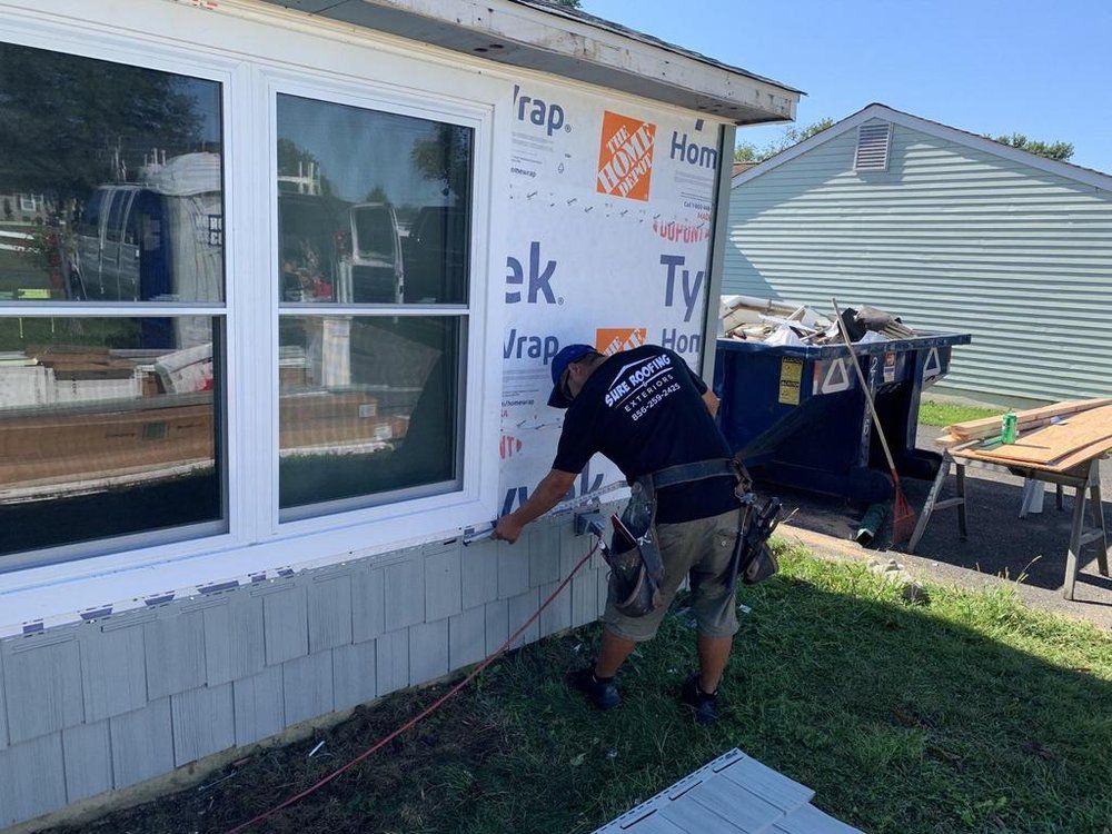 Worker installing siding on a house exterior with tools beside a window and porch.