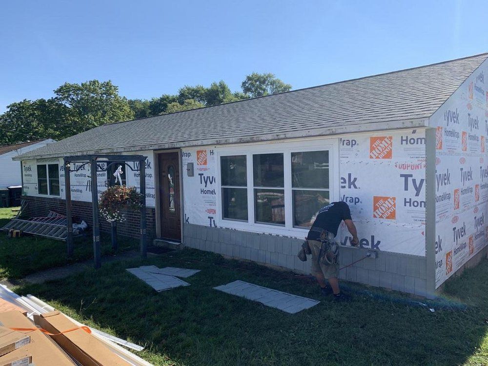 House under construction with Tyvek wrap and a worker painting the exterior trim.