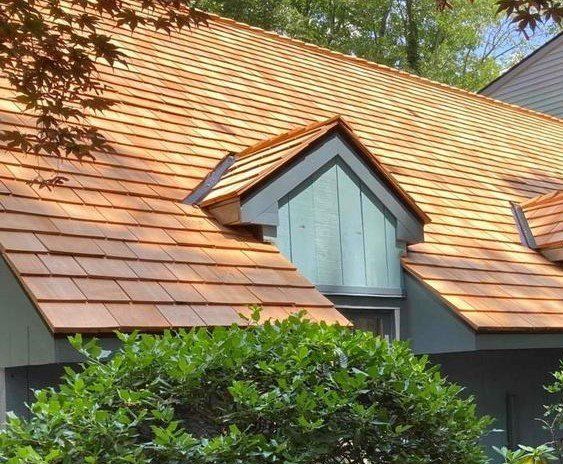 A copper-roofed house with a dormer window, partly hidden by shrubs and trees