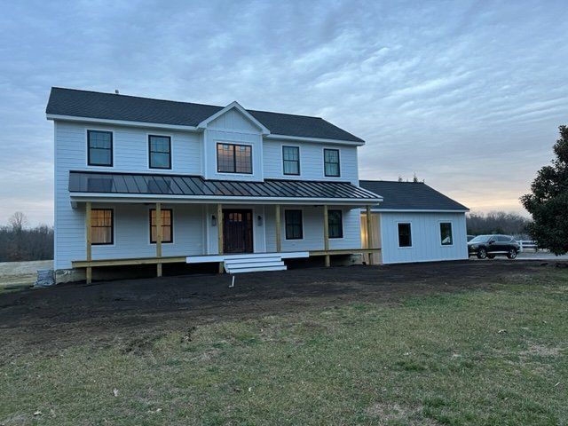 Two-story white farmhouse with a porch and detached garage at dusk on a grassy lot