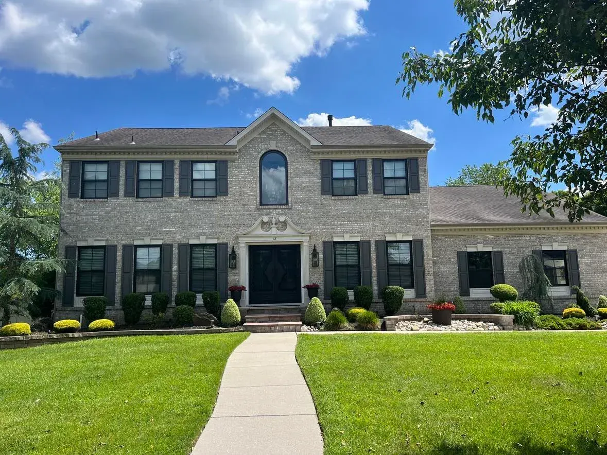 Two-story brick house with a front lawn, walkway, and blue sky with clouds