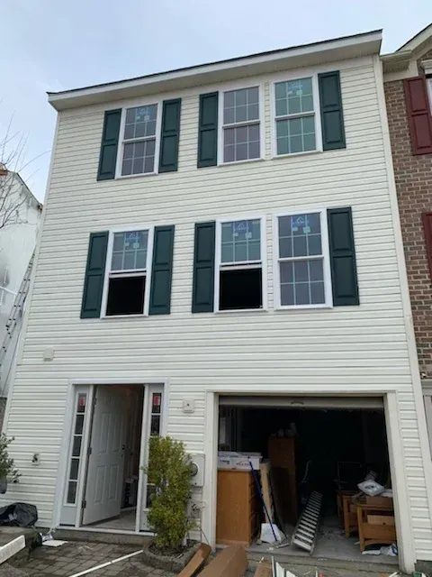 Three-story townhouse with open garage and white siding, viewed from the street