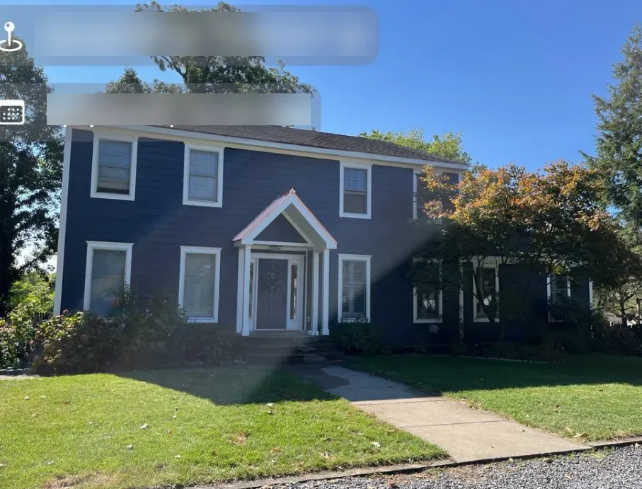 Blue two-story house with white trim, front lawn, and sidewalk under a sunny sky