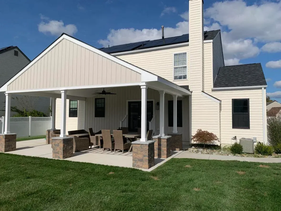 White house with a covered porch, brick columns, and green lawn under a clear sky