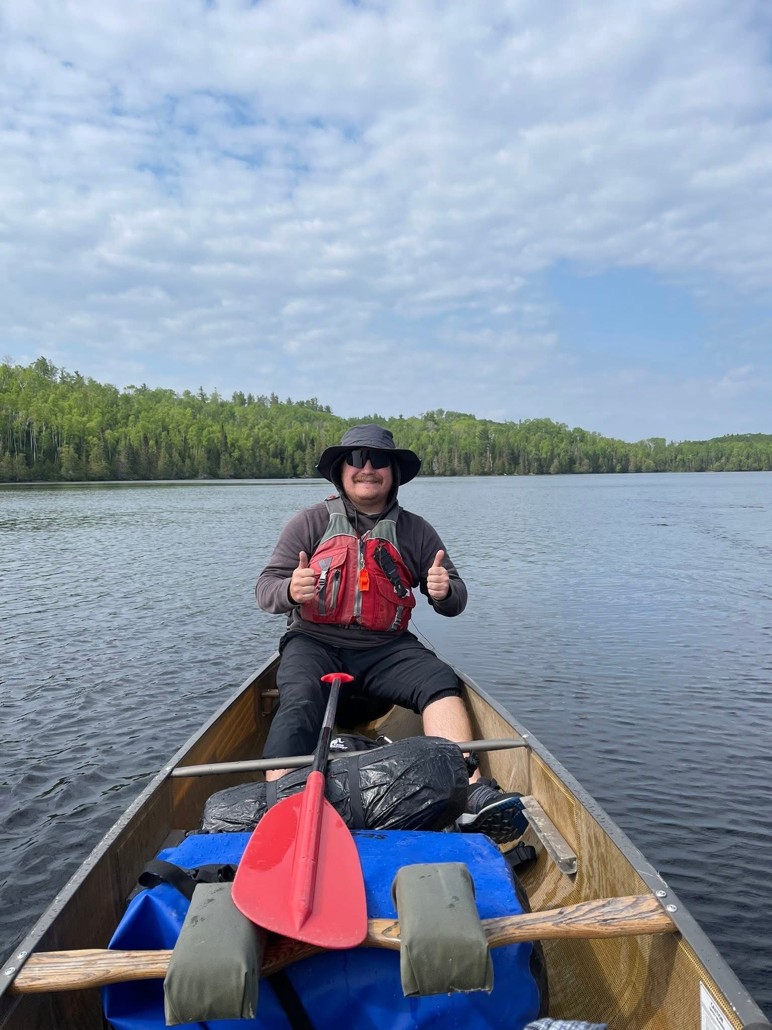 A man is sitting in a canoe on a lake giving a thumbs up.