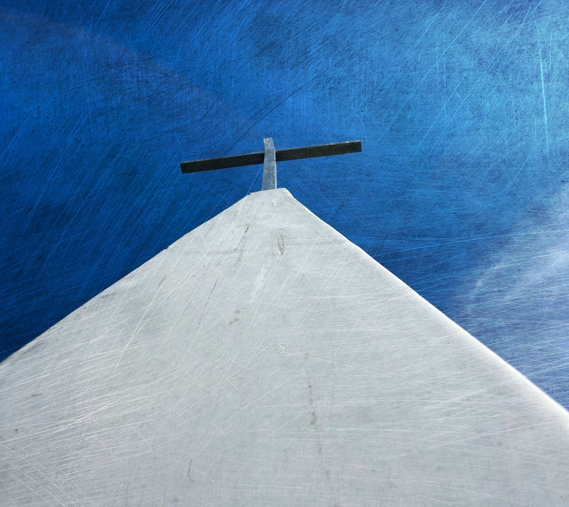 A cross on top of a white building with a blue sky in the background