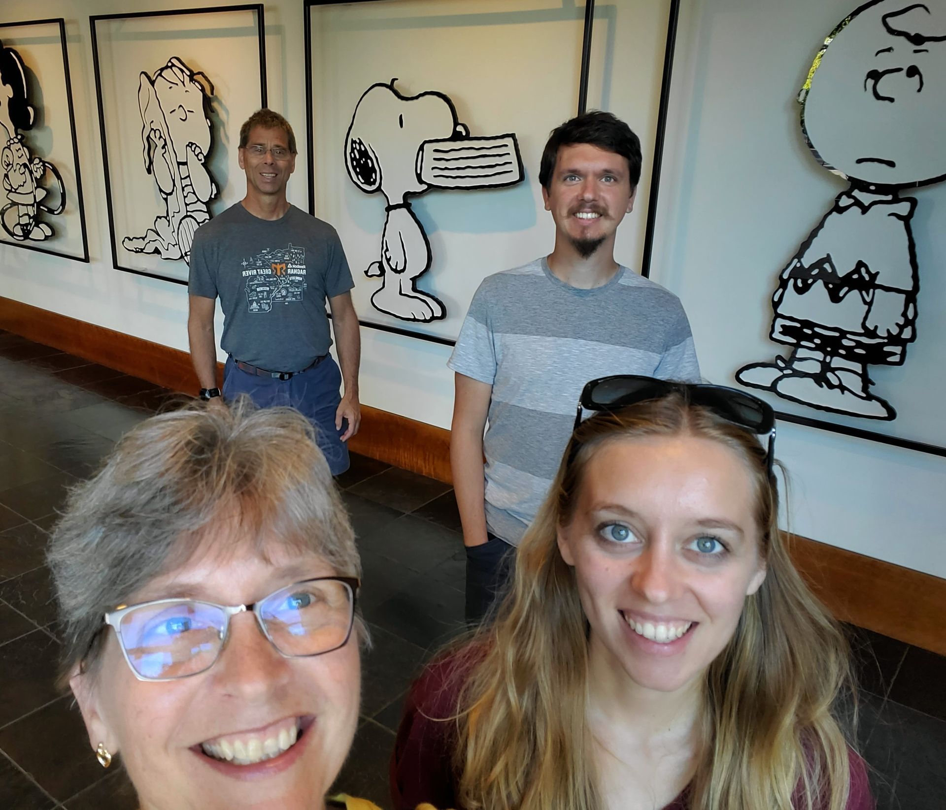 A group of people posing for a picture with snoopy and charlie brown in the background