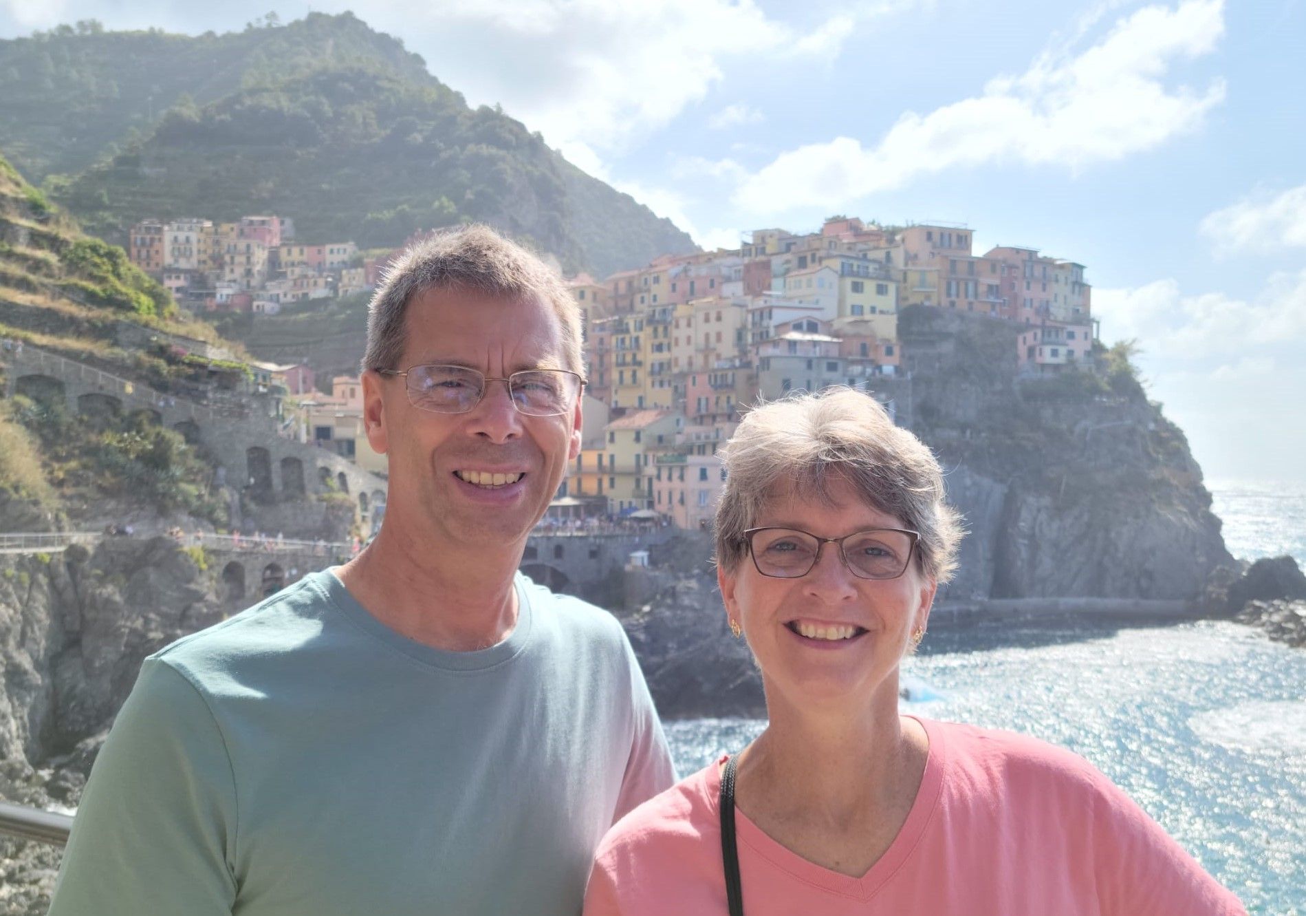 A man and a woman are posing for a picture in front of a cliff overlooking the ocean.