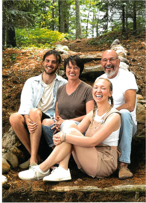 A family is posing for a picture while sitting on steps in the woods.