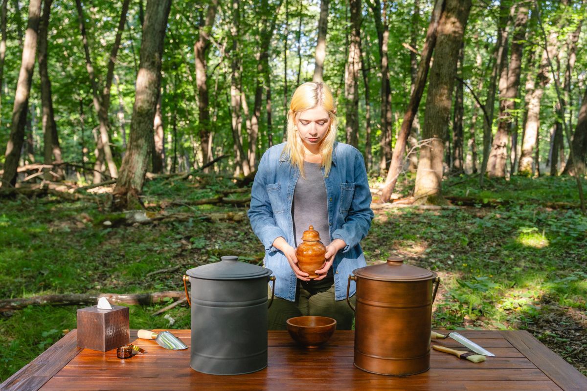 Woman with an urn in her hands standing in front of a table with two canisters on it and some gardening tools at Better Place Forests in Minnesota