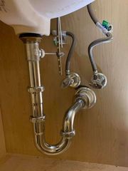 Under-sink plumbing with chrome drain pipes and flexible water supply lines beneath a sink
