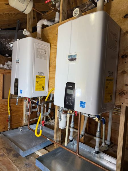Two white wall-mounted water heaters in a utility room with exposed pipes and ductwork.