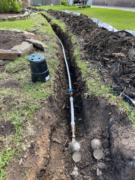 Trenched yard with a buried pipe and valve running through grass beside a dug-up soil mound