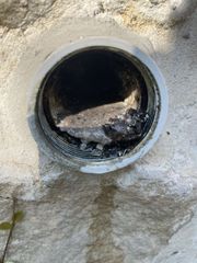 Round concrete drainage opening in a rough beige wall, with dark interior and debris inside
