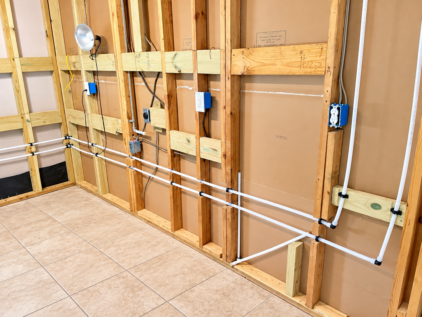 Six vertical white pipes against a speckled gray wall, with small rust stains and orange clips.