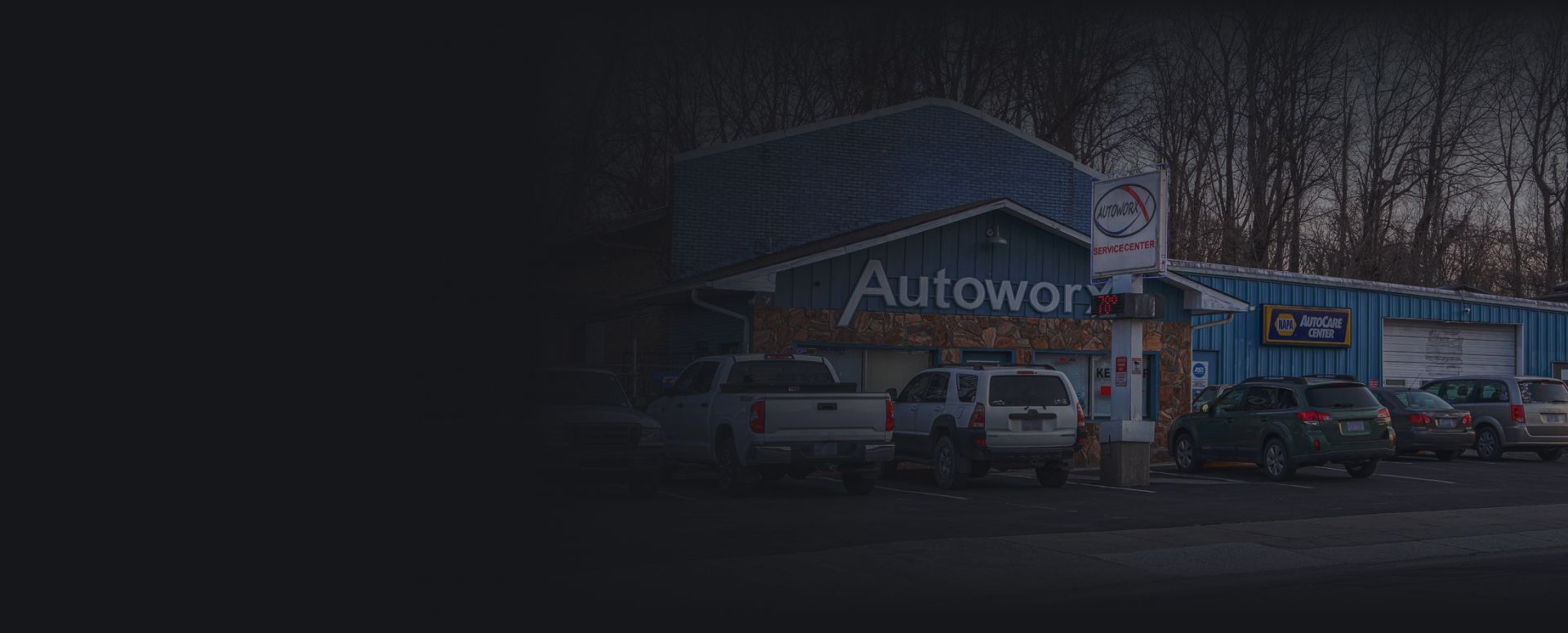 Dim storefront with parked cars and a blue building sign reading “Autoworld” | Autoworx