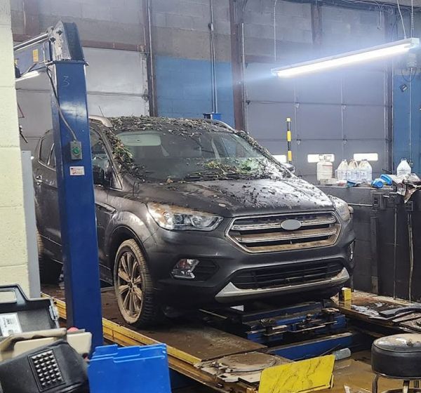 Dark gray SUV on a lift in an auto repair shop, with debris on the hood and windshield. | Autoworx
