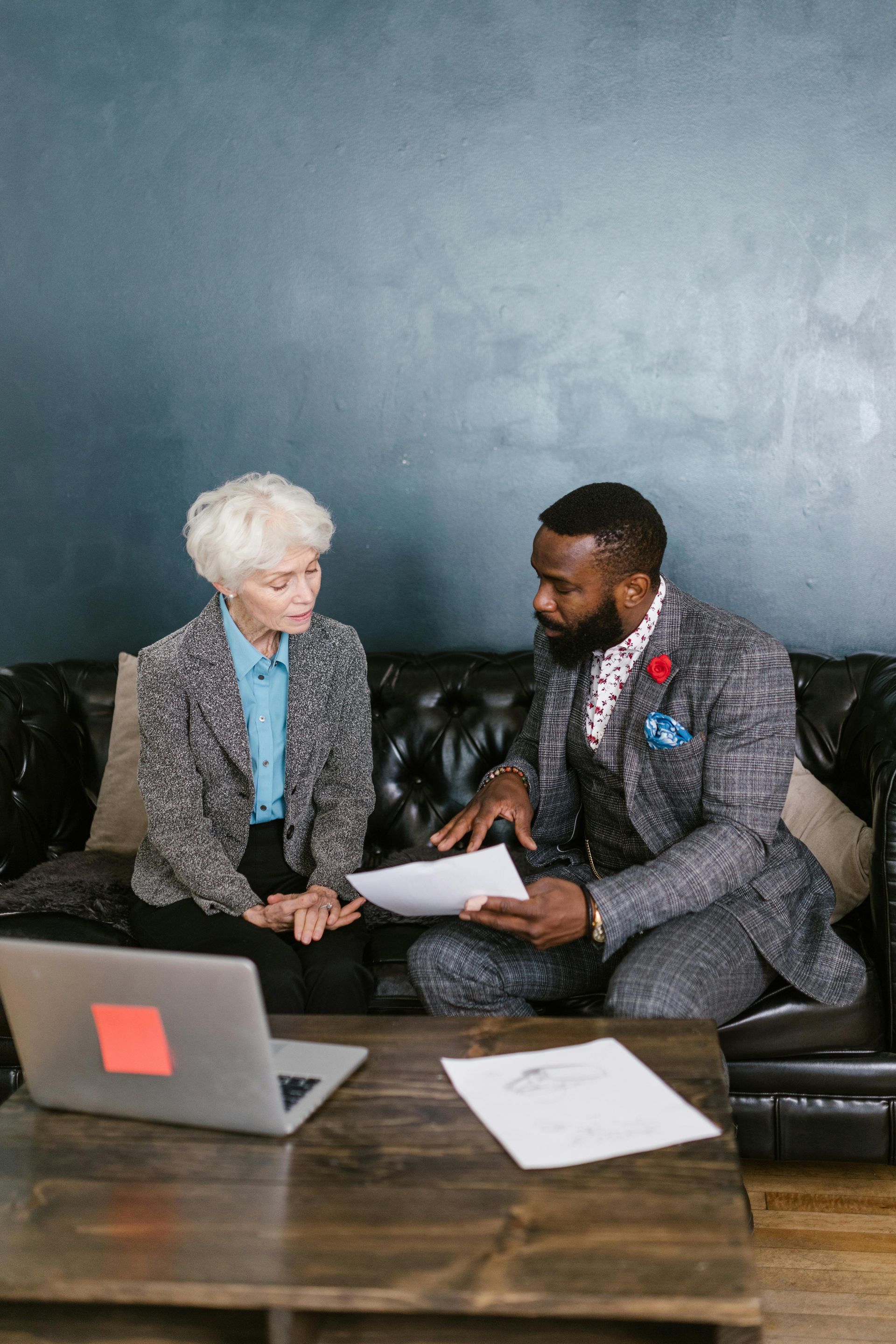 Two people discussing papers on a couch beside a laptop and coffee table in a modern office lounge
