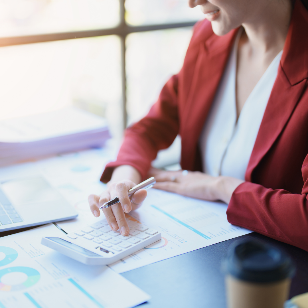 A woman is sitting at a desk using a calculator and a pen.