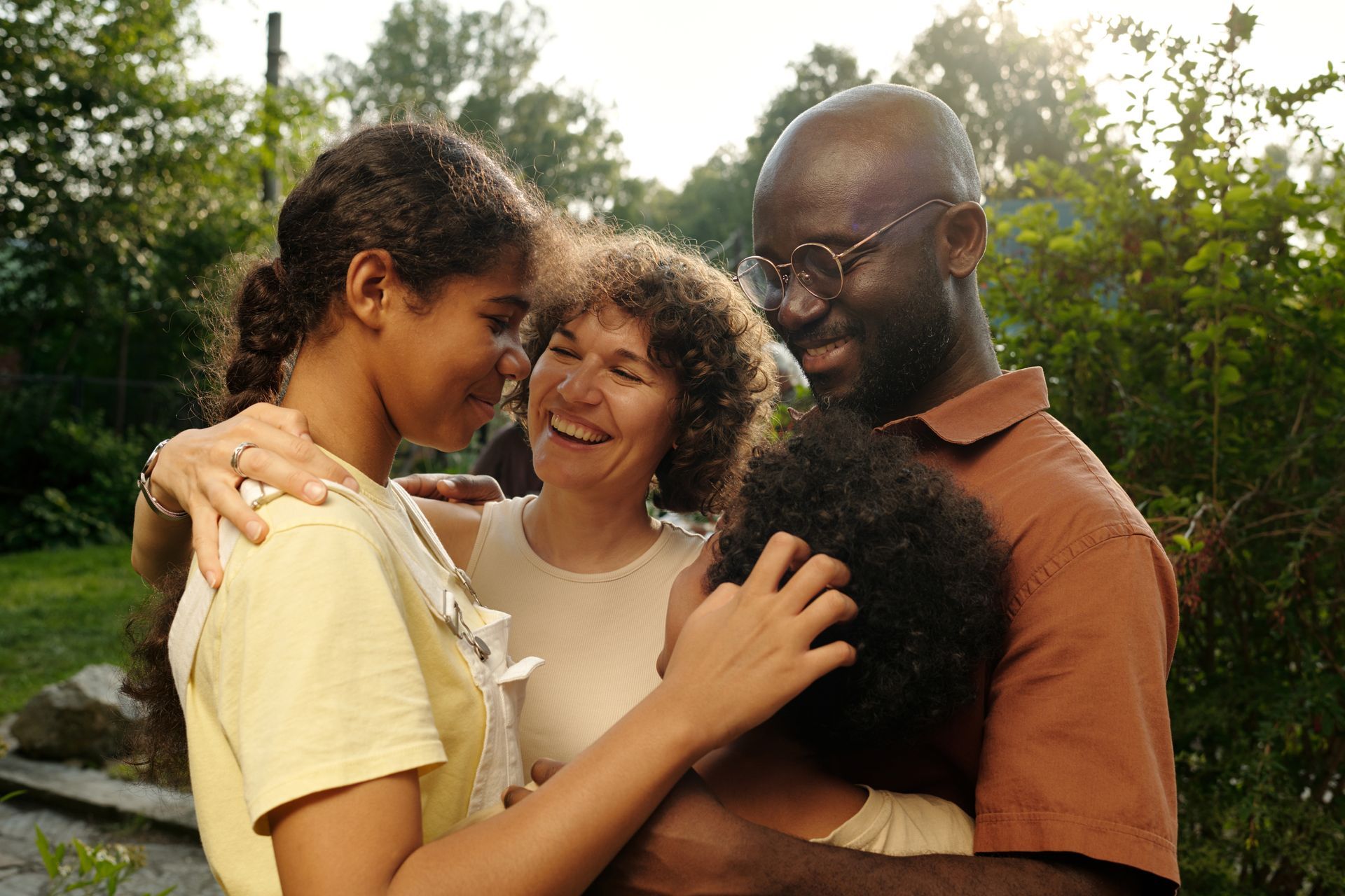 Family embracing outdoors, laughing, and smiling. Warm lighting, green foliage.
