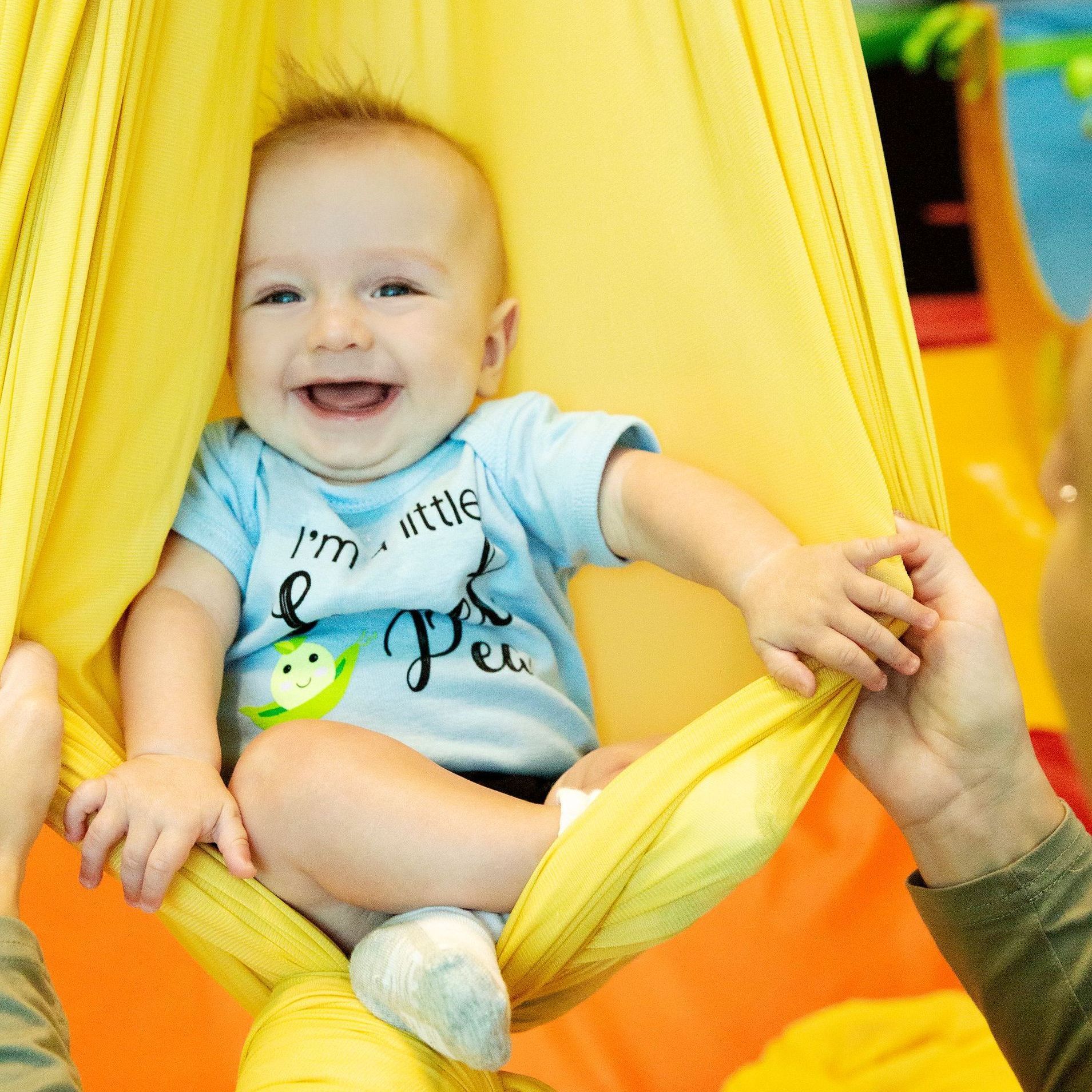 Smiling baby in a yellow hammock swing being held up by hands