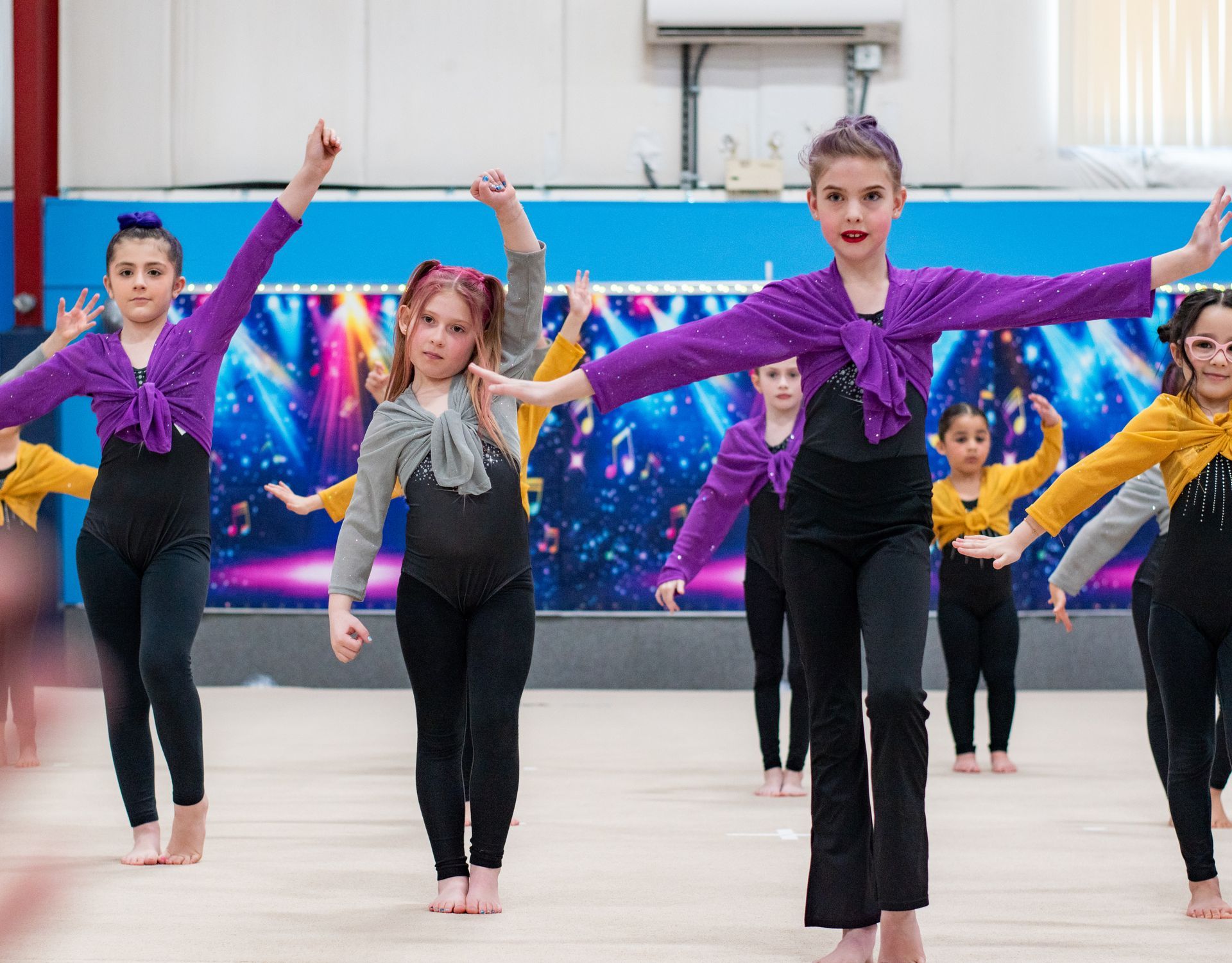 Children performing a dance routine in matching purple tops on a gym floor.