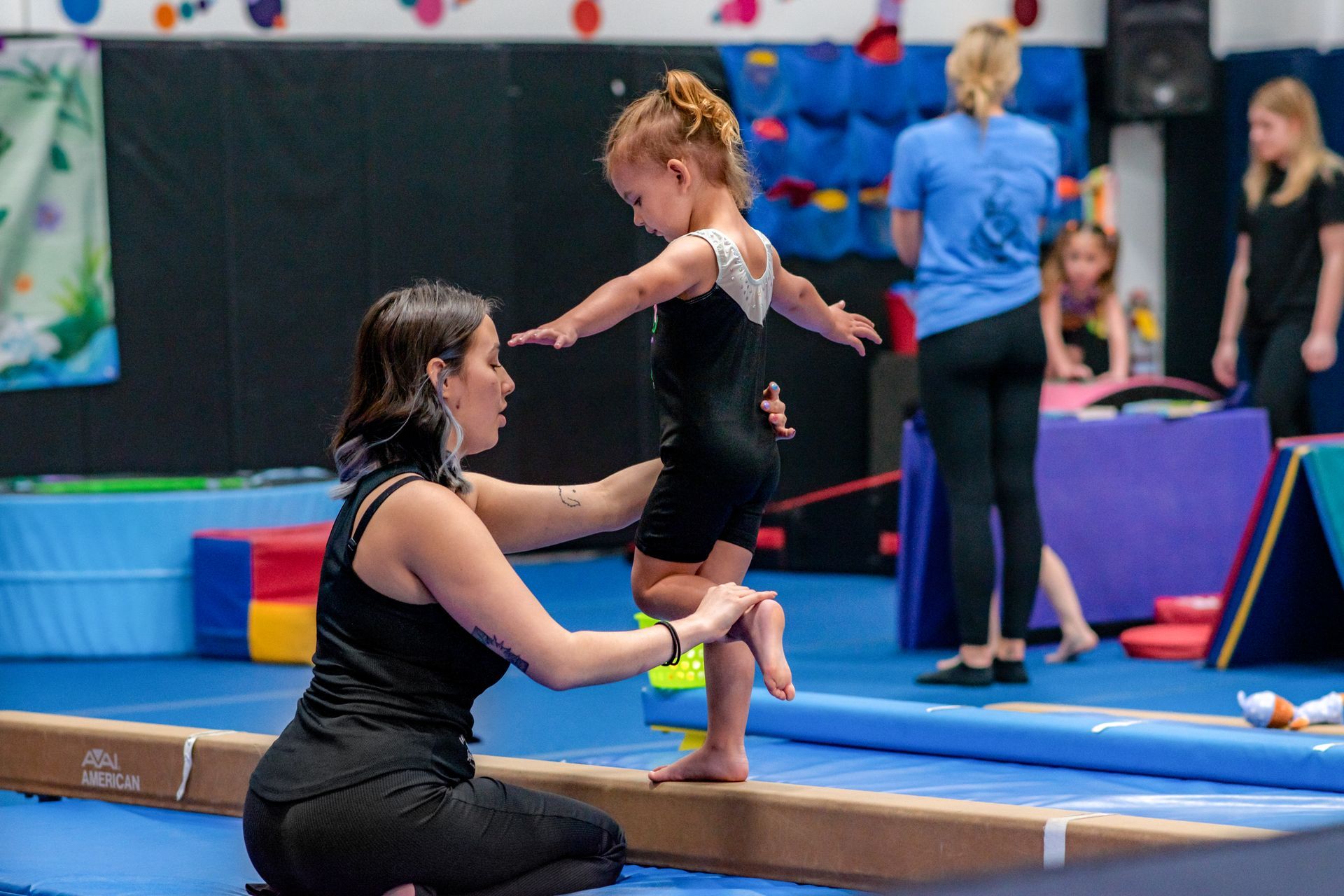 Gymnastics coach helping a child balance on a beam in an indoor gym